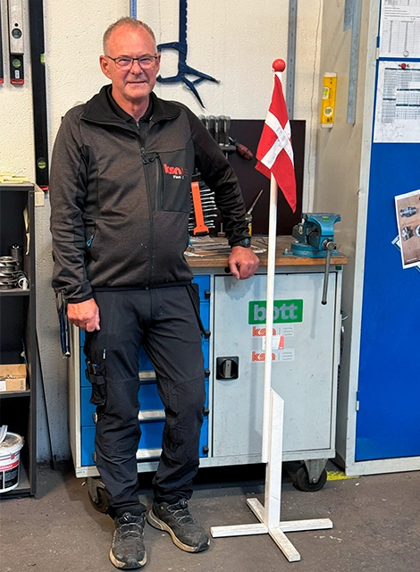 Finn Dalby står ved et dansk flag på sin arbejdsplads hos KSN i forbindelse med fejringen af sit 35-års jubilæum.